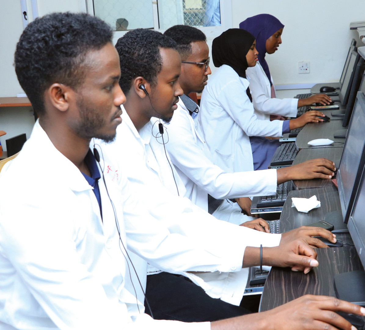 Learners in white coats working at computers during online teaching.